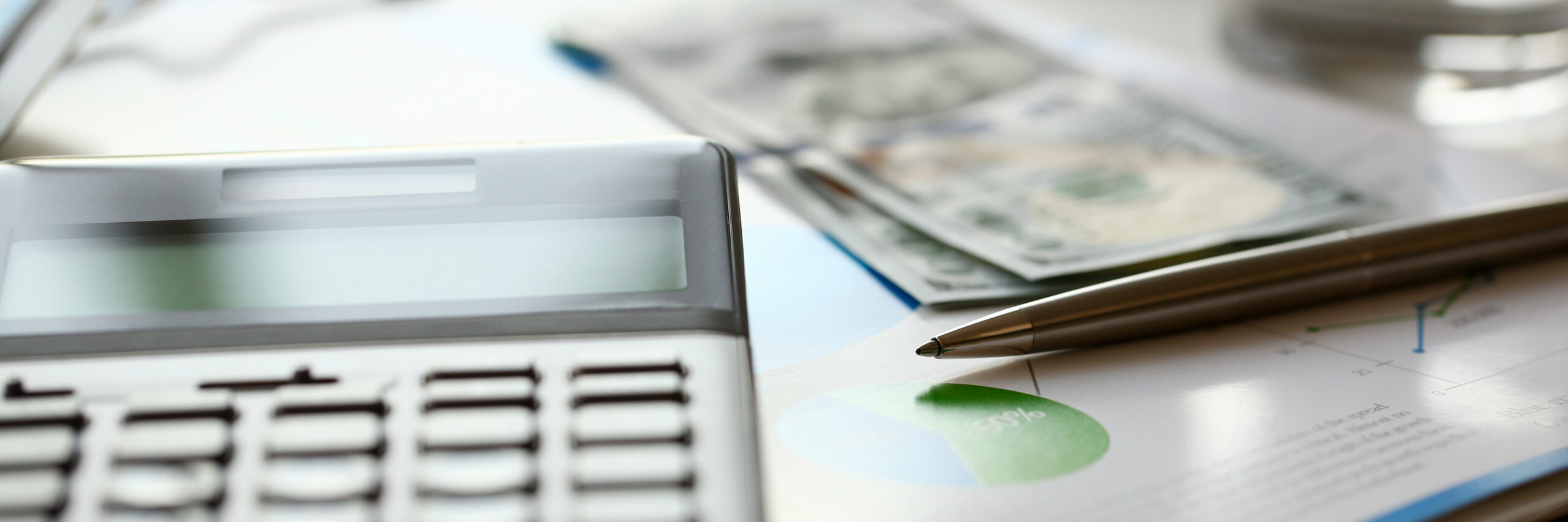 A close-up photo of a calculator, some dollar bills and a pen.